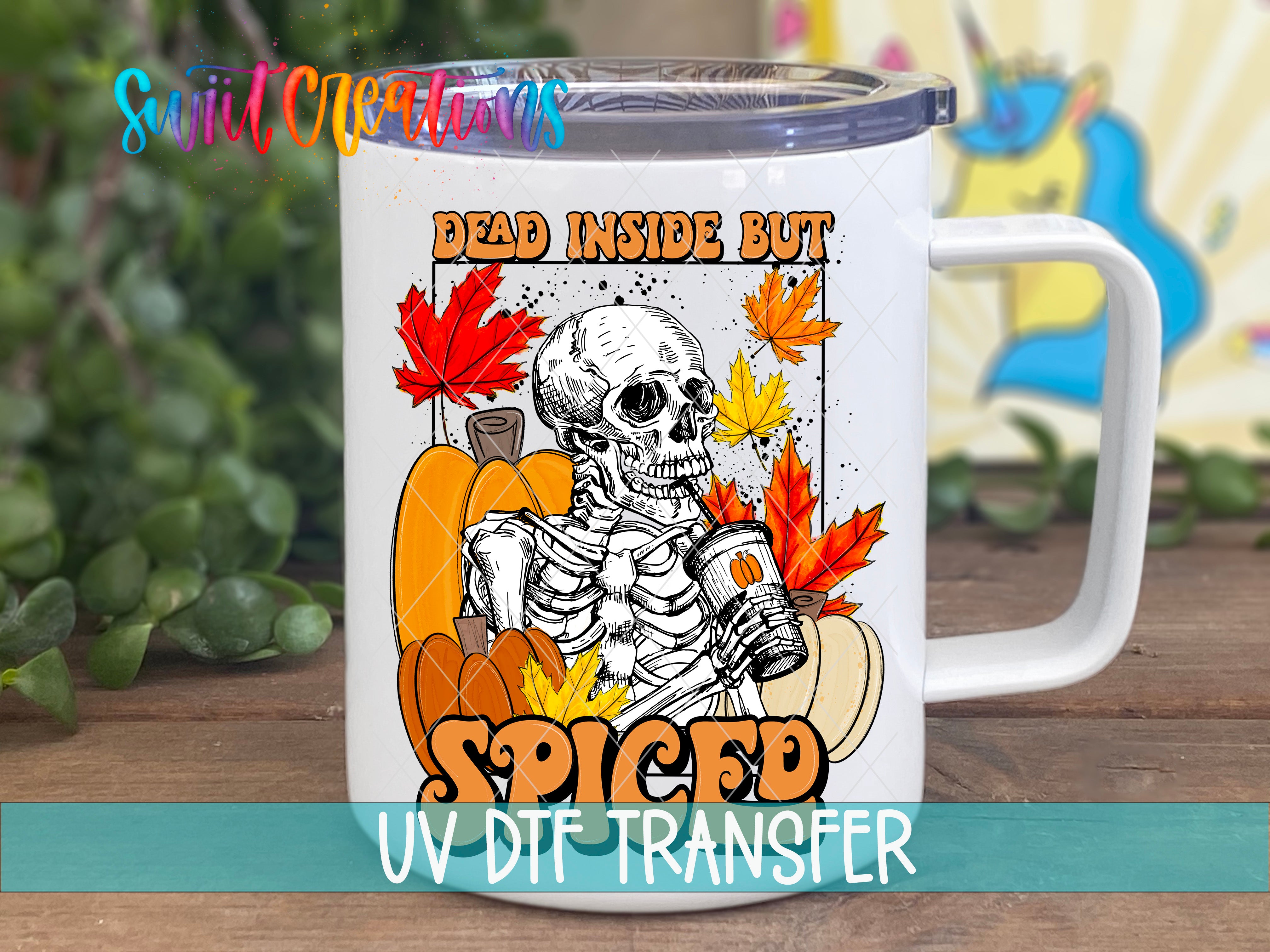 A white mug with a printed design featuring a skeleton holding a cup, surrounded by autumn leaves and pumpkins, with the text "Dead inside but Spiced" and "UV DIE TRANSFER" printed on it.