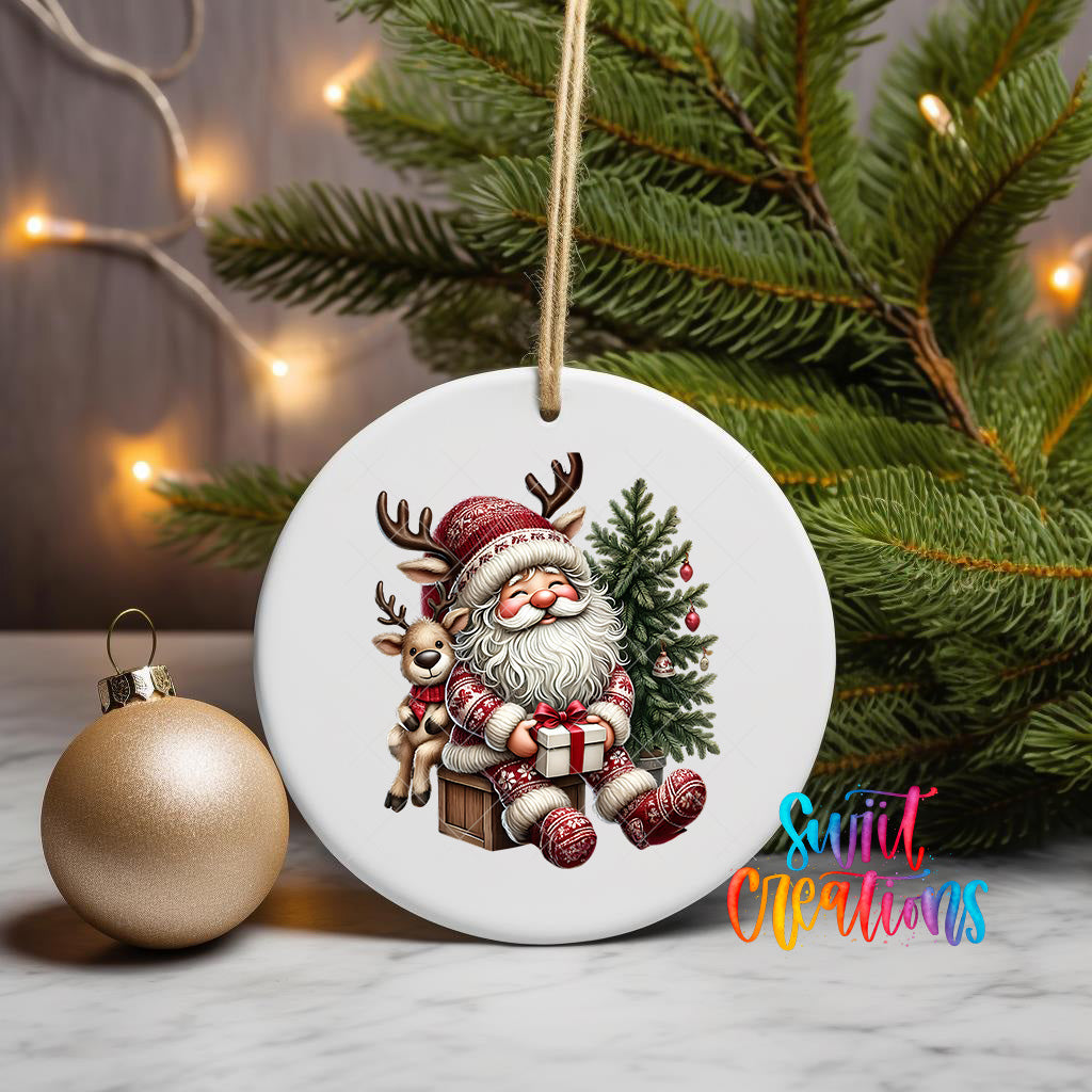 A white ceramic ornament featuring a smiling Santa Claus holding a reindeer and a Christmas tree, with a gold ornament and a pine tree in the background.