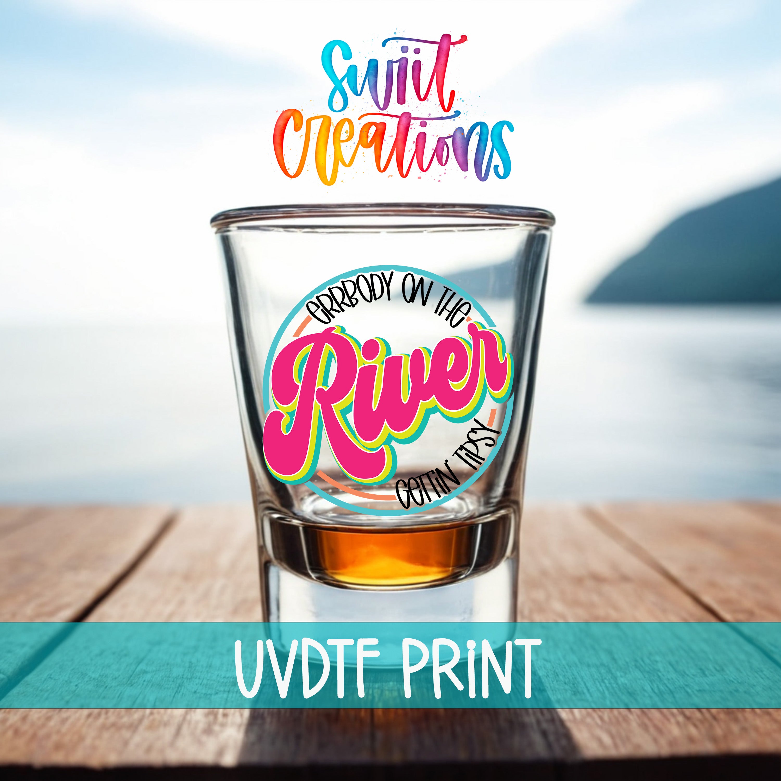 a shot glass with a colorful design on it, placed on a wooden surface with a body of water in the background.