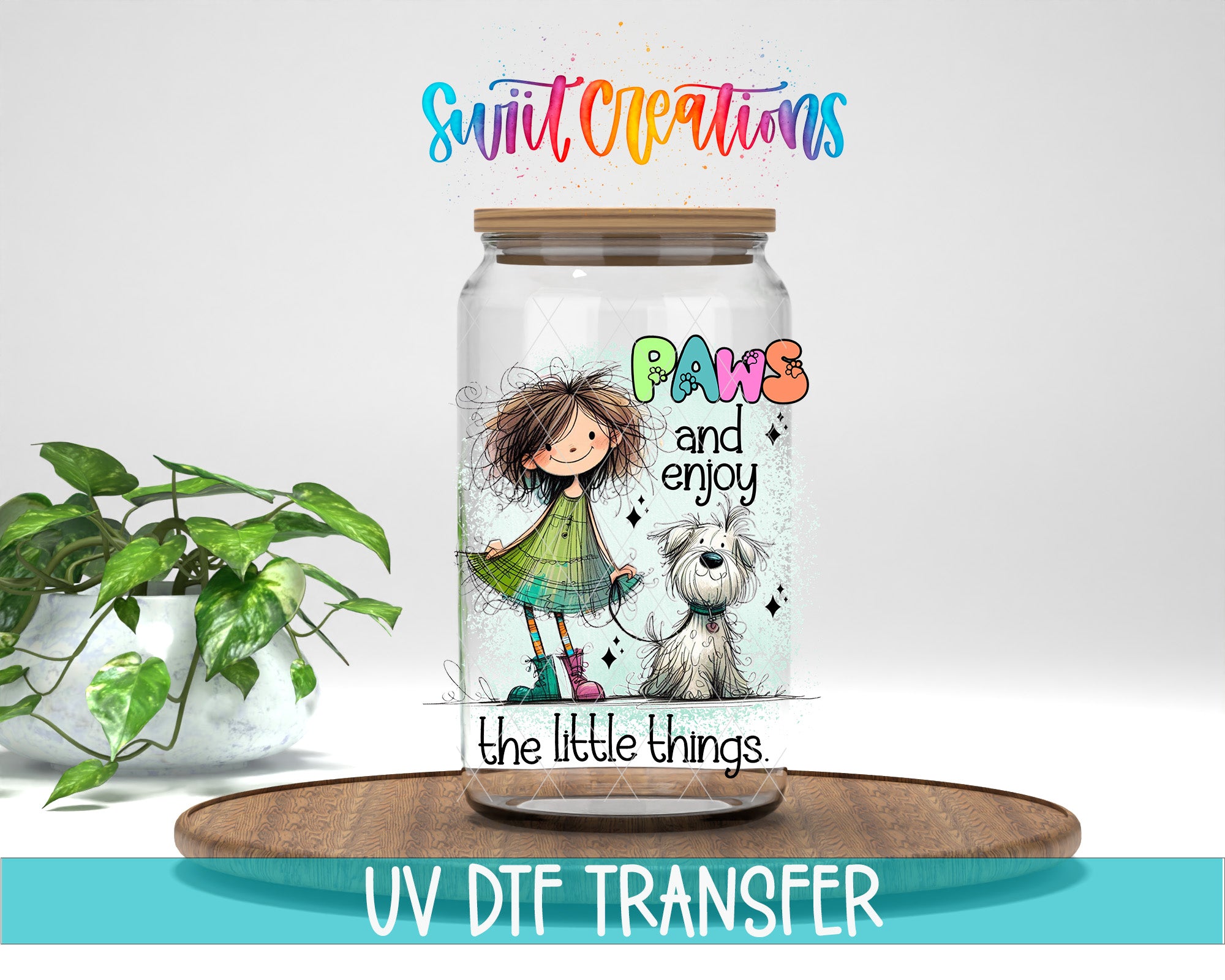 A glass jar with a colorful illustration of a girl and a dog, along with the text "Paws and enjoy the little things" and "Swift Creations". The jar is placed on a wooden surface, and there is a potted plant in the background.