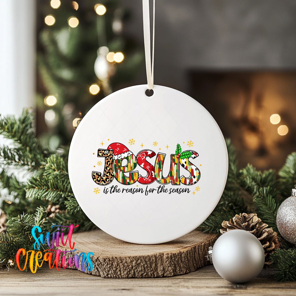A white ceramic ornament with the word "Jesus" written on it, surrounded by Christmas decorations such as pine cones and ornaments.