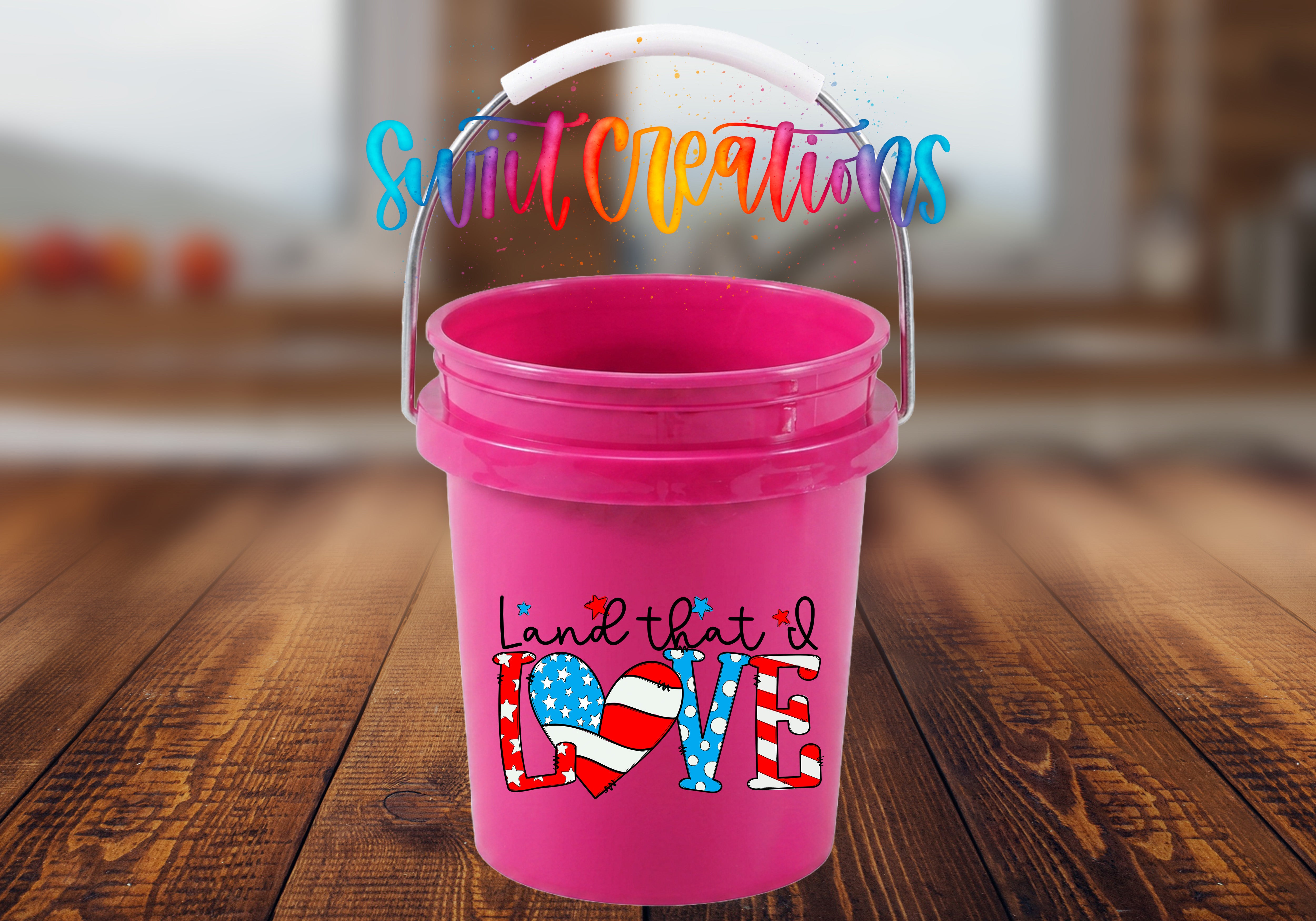 A pink bucket with a handle and a colorful, stylized text design on it, placed on a wooden surface.