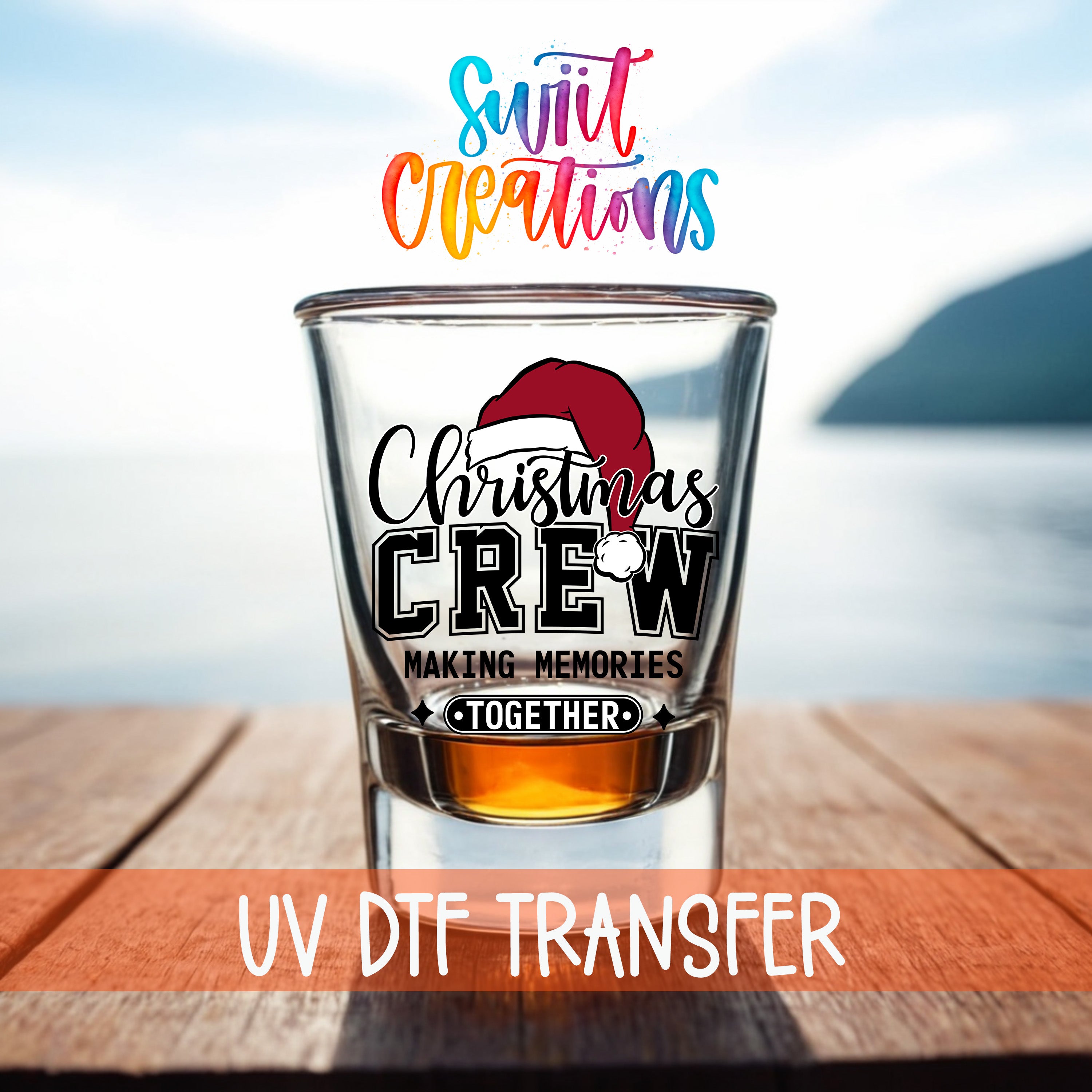 A shot glass with a Christmas crew design on it, placed on a wooden surface with a body of water in the background.