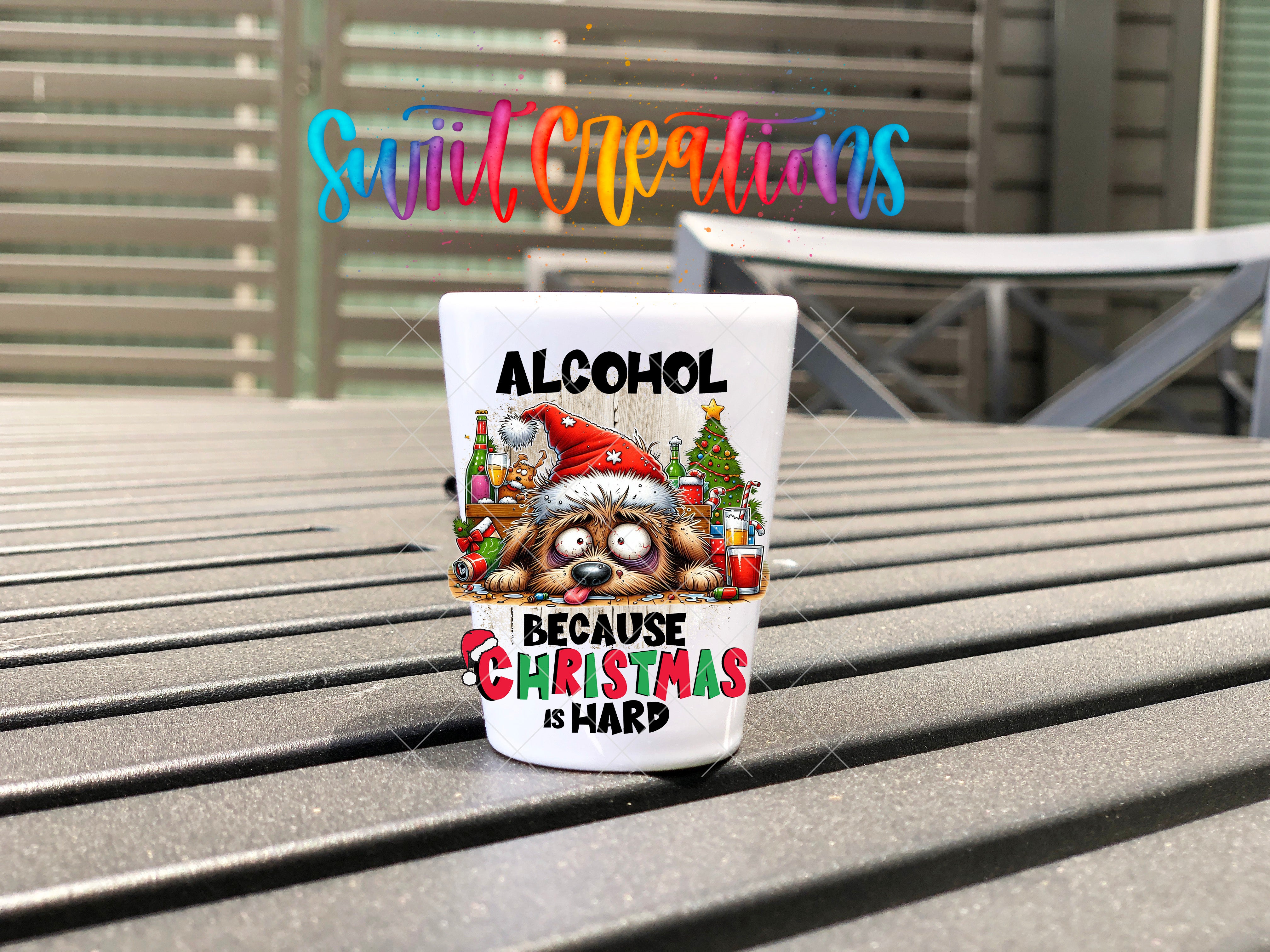 A shot glass with a Christmas-themed design and text on it, placed on a wooden surface.