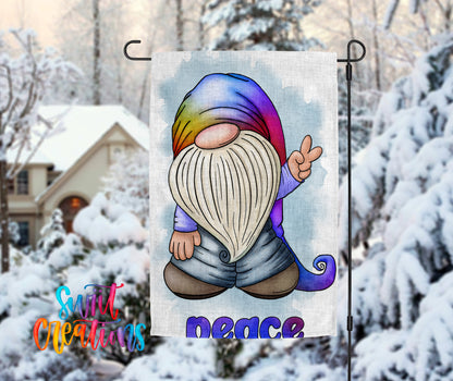 A colorful garden gnome waving peace signs is displayed on a flag, with a snowy winter landscape in the background.