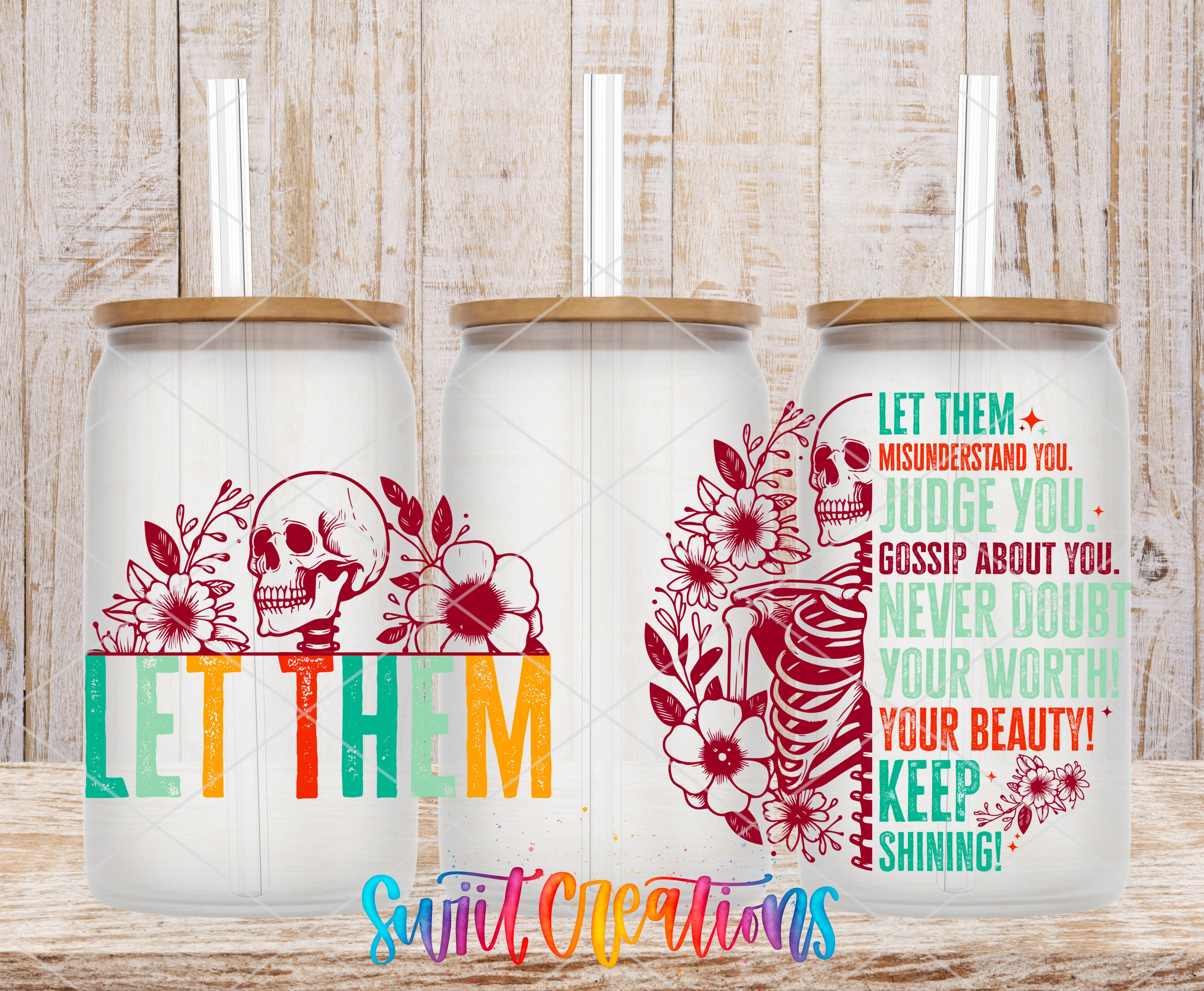 A colorful glass can with a lid and straw, featuring a skull and floral design. The can also has text and a motivational quote on it.