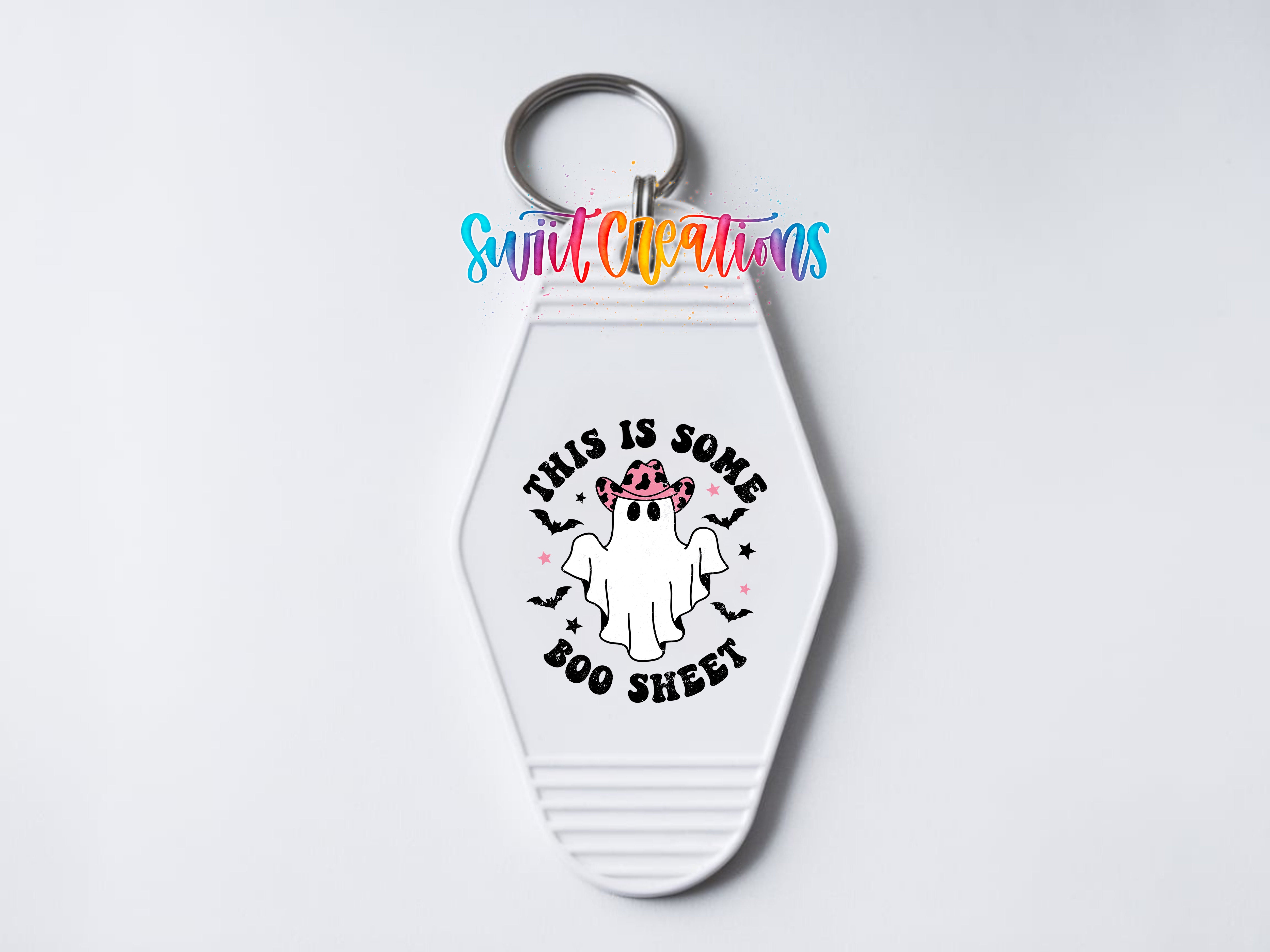 A white keychain with a graphic design featuring a ghost wearing a pink hat and the text "This is some BOO sheet" printed on it.