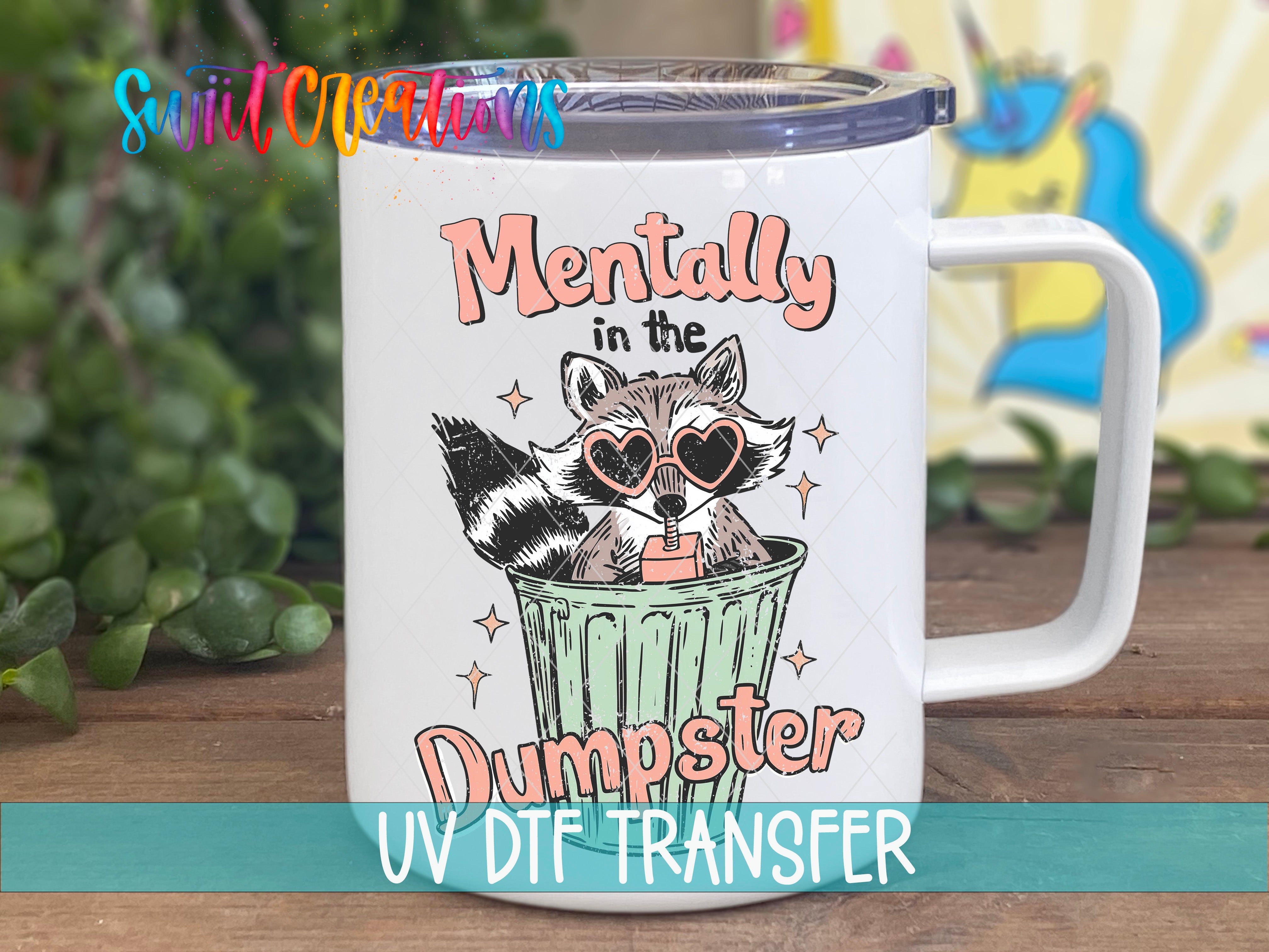 A white mug with a colorful design featuring a raccoon wearing sunglasses and the text "Mentally in the Dumpster" printed on it.
