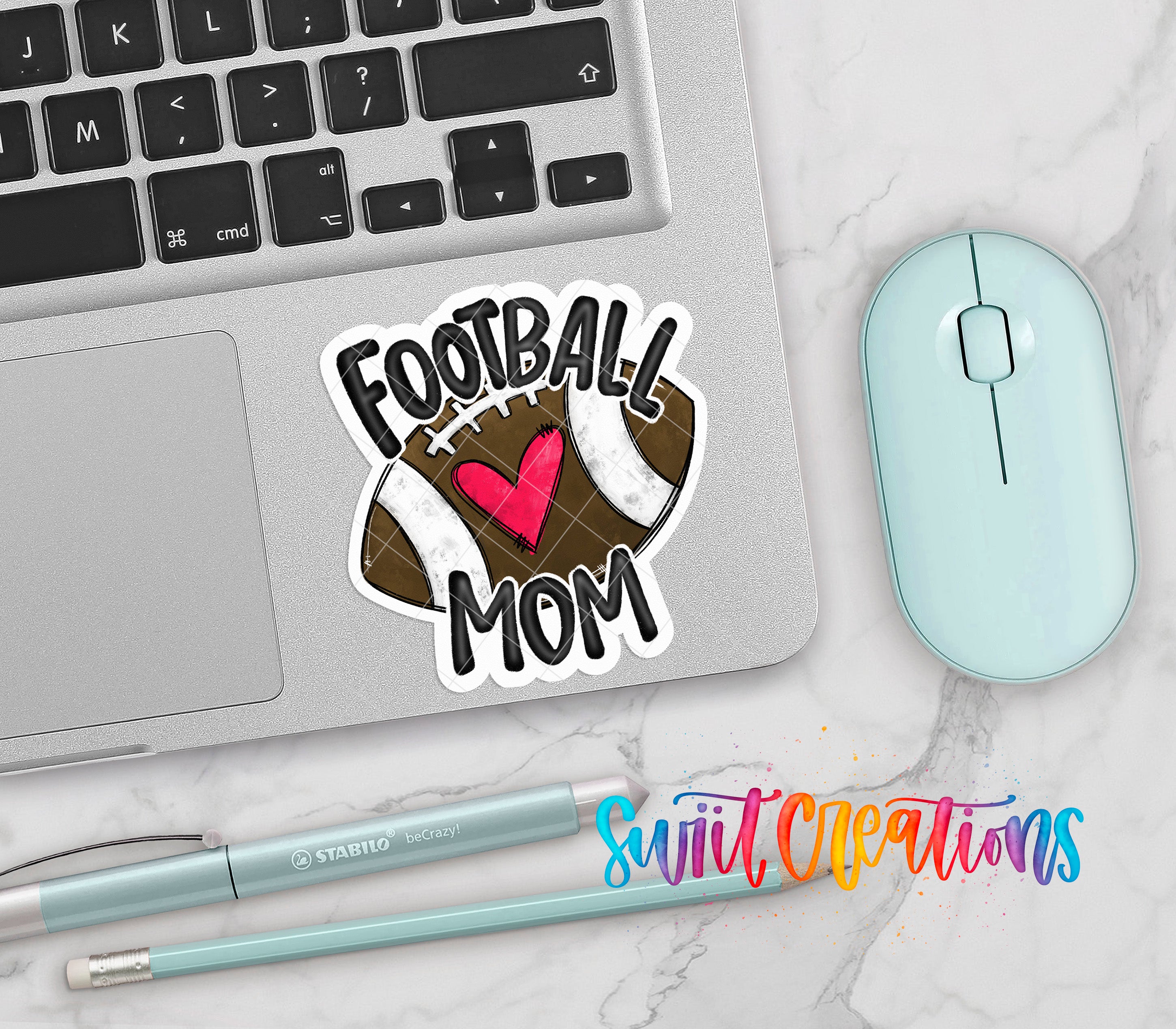 a laptop with a sticker that says "Football Mom", a mouse, a pen, and a pencil on a marble surface.