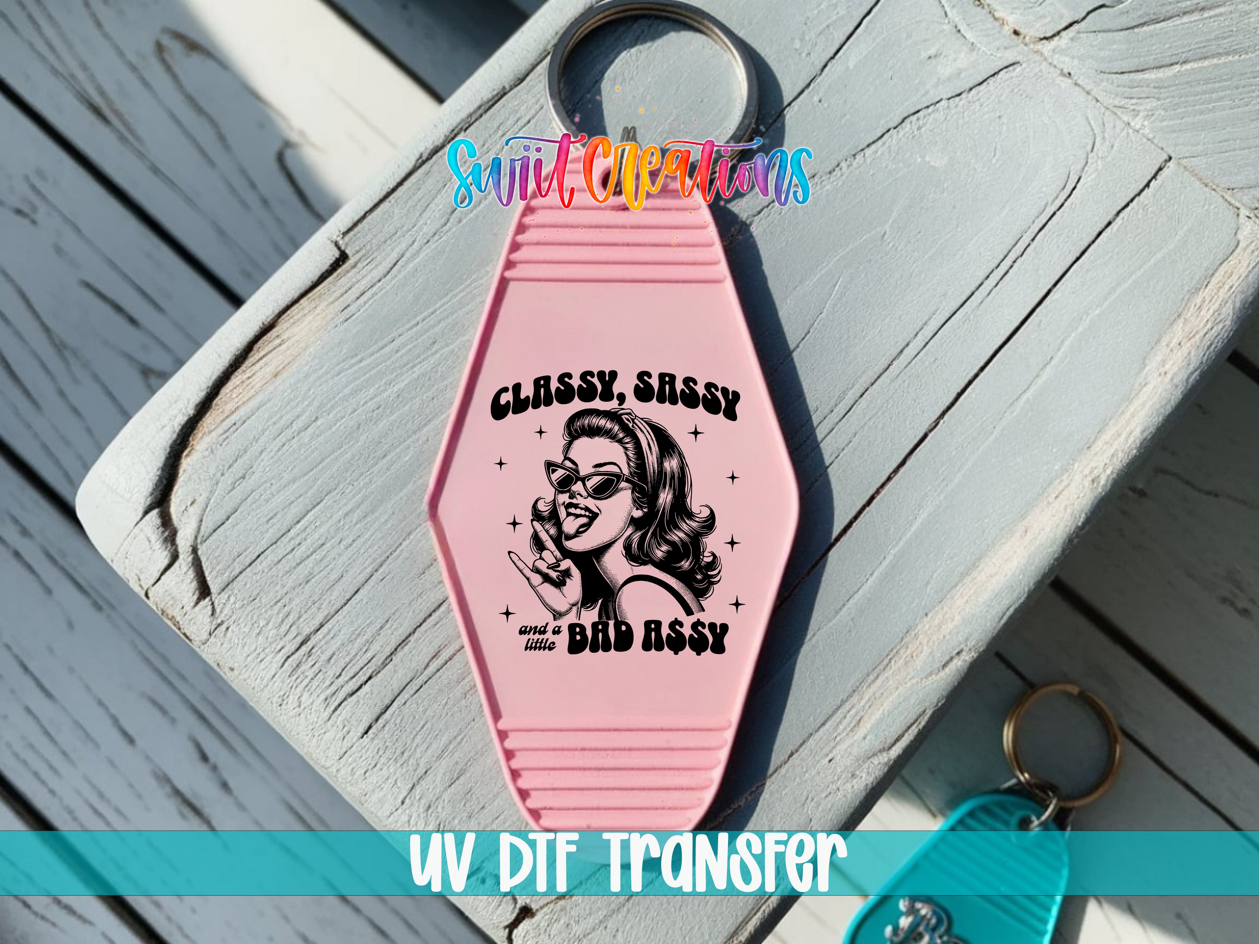 A pink keychain with a graphic design and text, placed on a wooden surface.