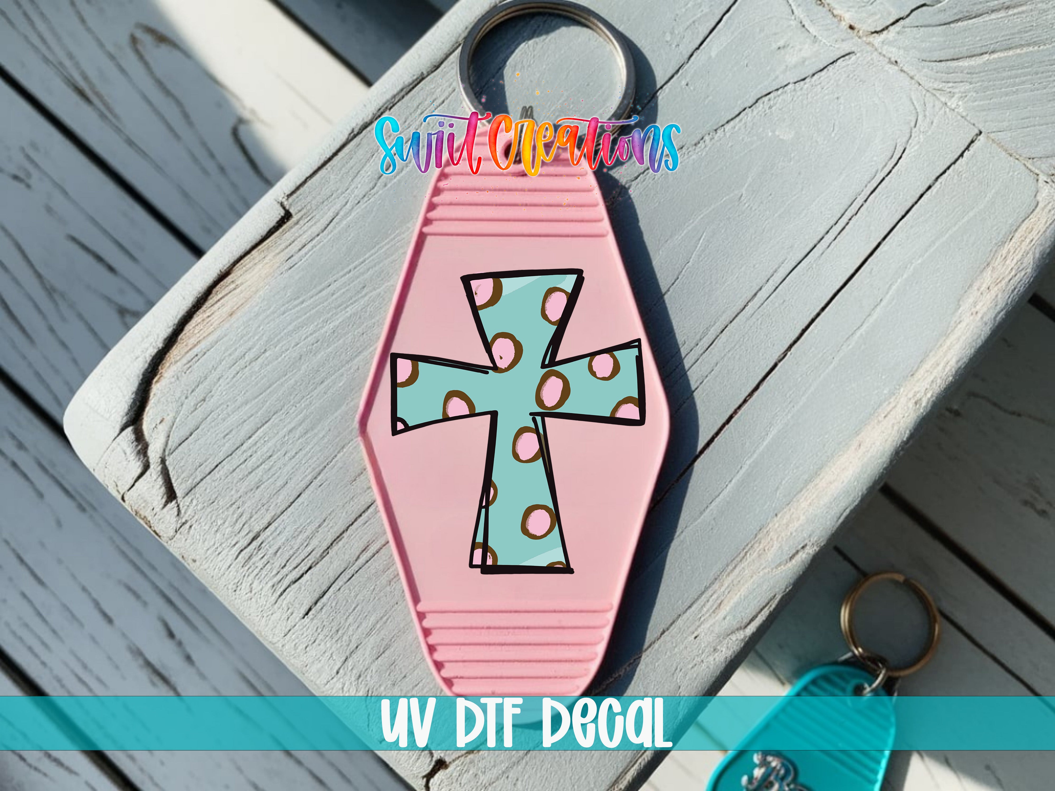 A pink keychain with a cross design and colorful polka dots is shown on a wooden surface.