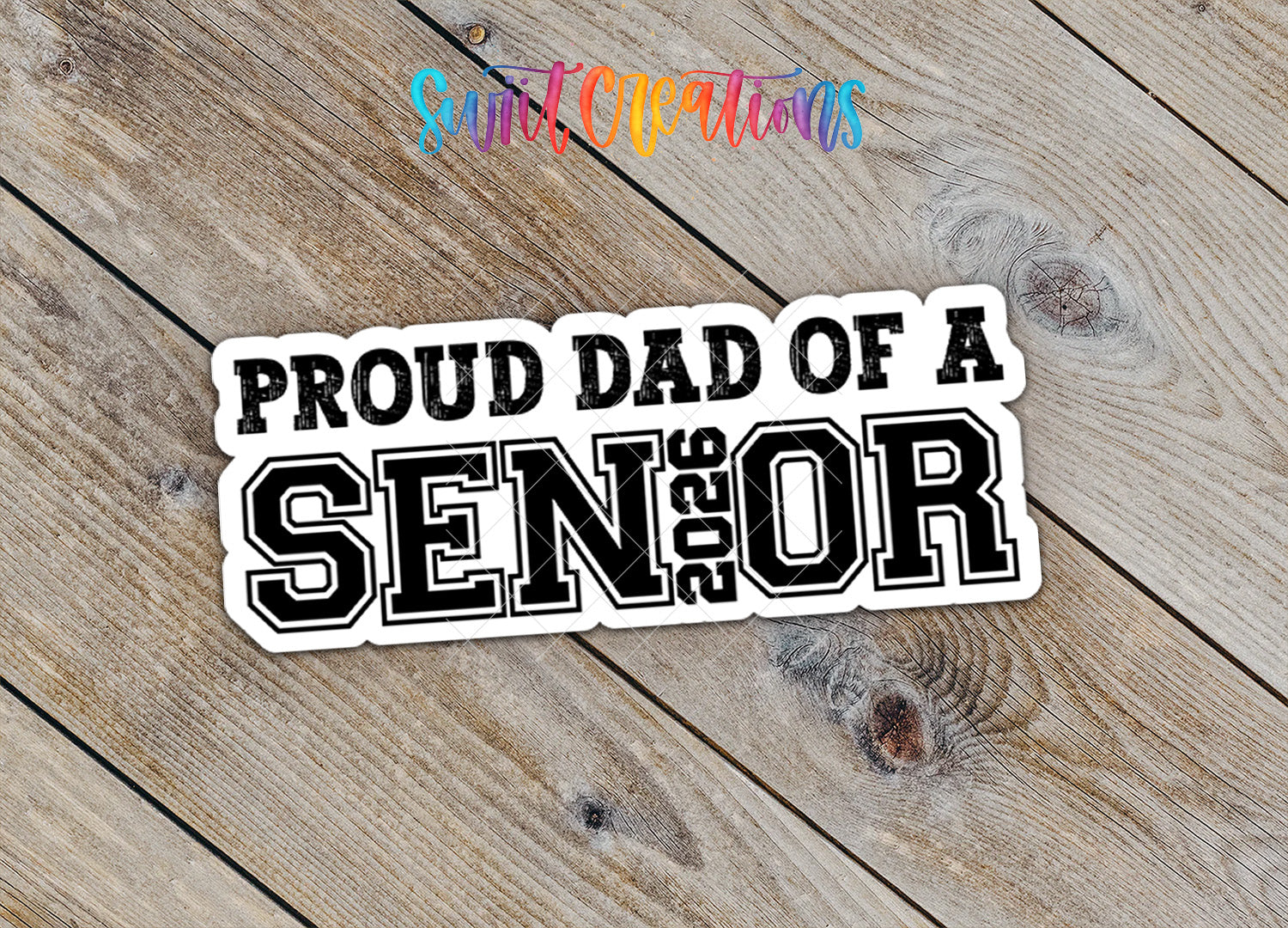 A sticker with the text "Proud Dad of a SENIOR" printed on it, placed on a wooden surface.