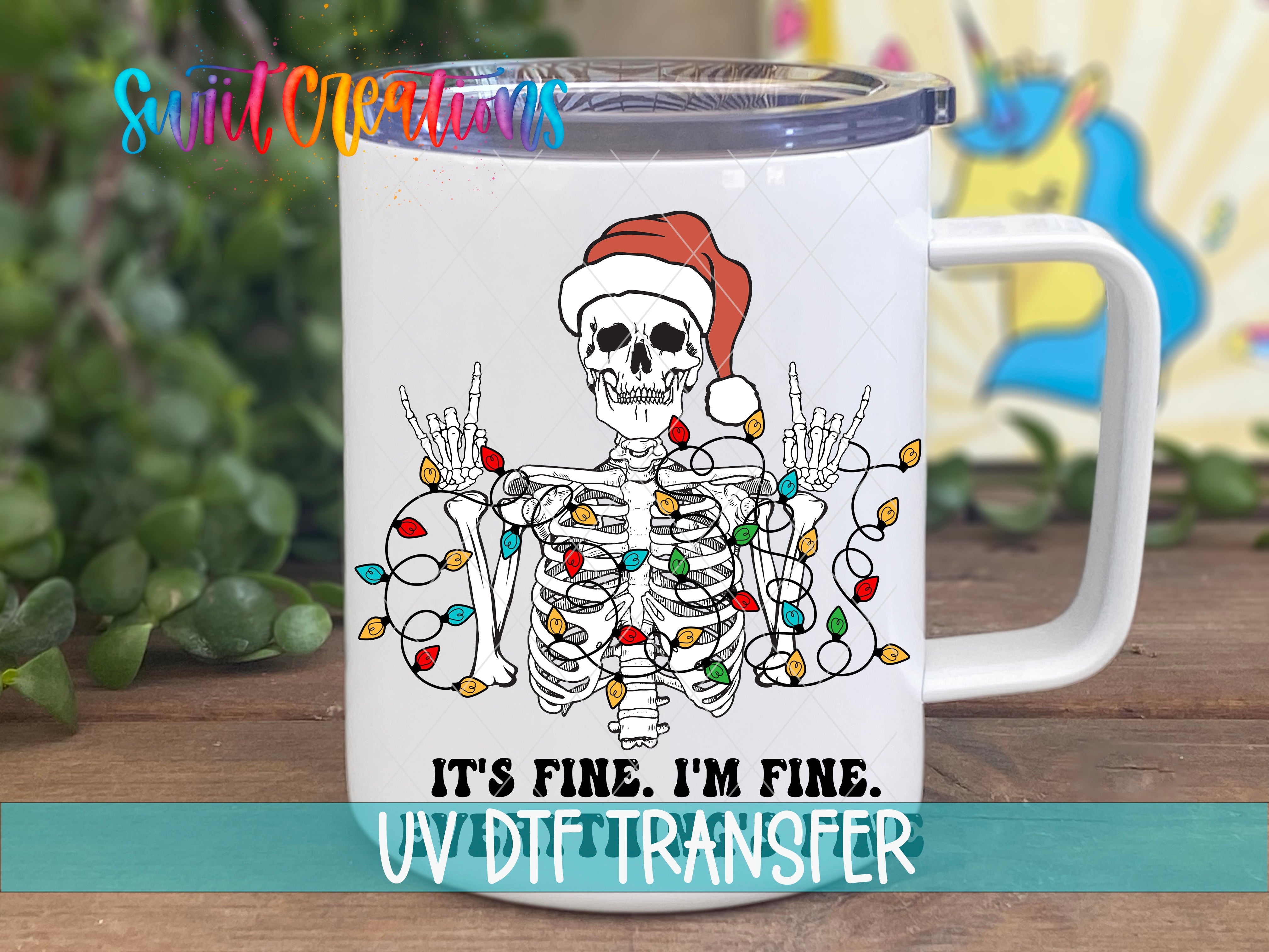 A white mug with a skeleton wearing a Santa hat and holding up Christmas lights, accompanied by the text "IT'S FINE, I'M FINE. UV DIFFERNER".