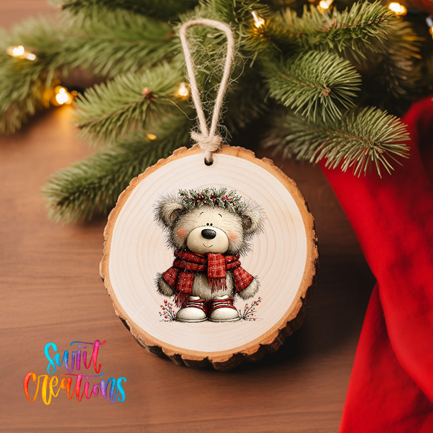 A wooden ornament featuring a teddy bear wearing a red scarf and a wreath, hanging on a Christmas tree.