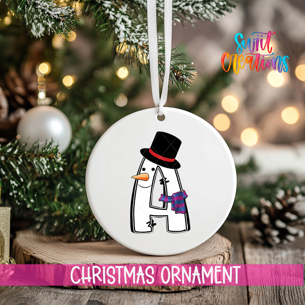 A white Christmas ornament with a snowman design hangs on a tree branch, surrounded by other ornaments and lights.