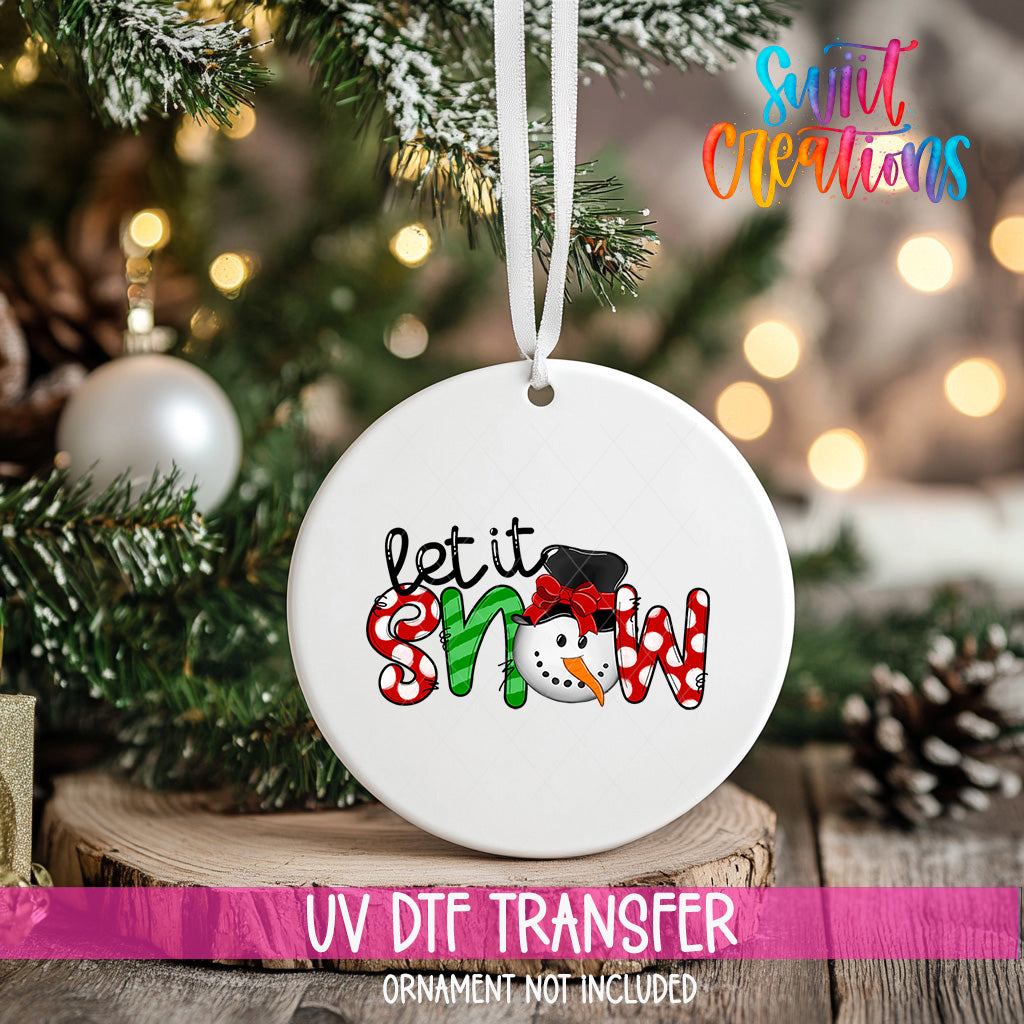 A white ornament with the text "let it snow" and a snowman graphic hangs on a Christmas tree.