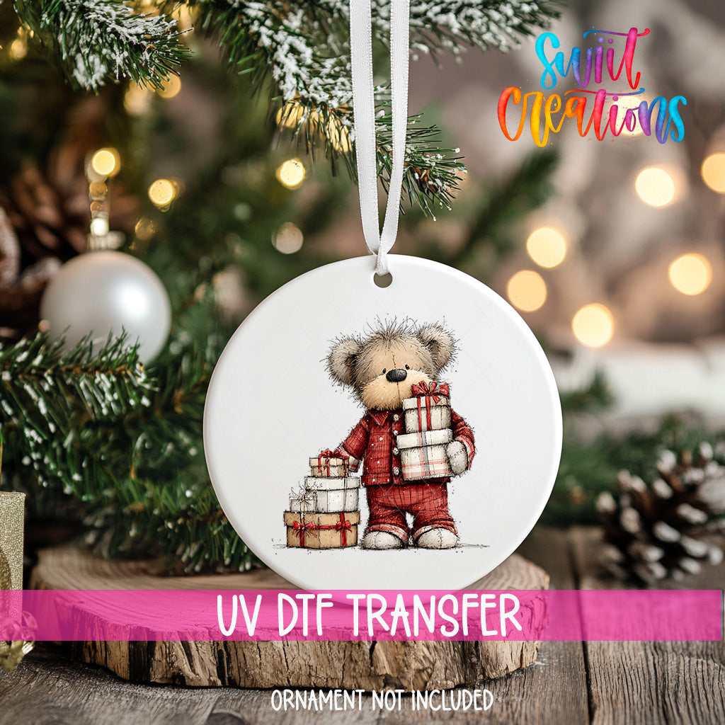 A white ornament with a teddy bear holding presents is hanging on a Christmas tree.