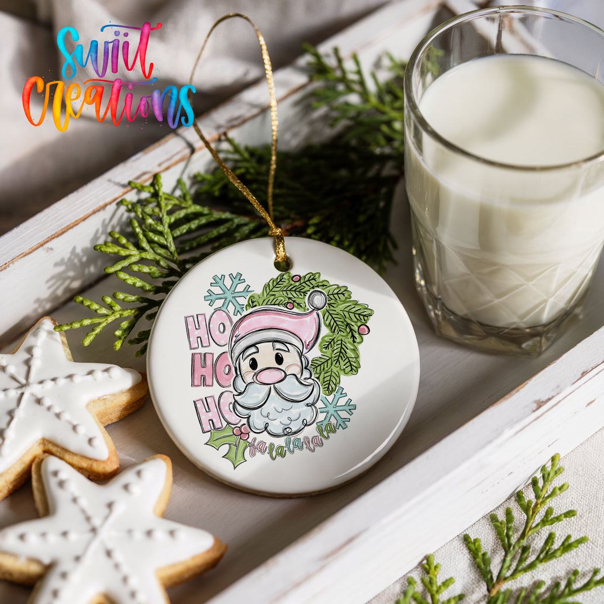 a festive scene with a Santa Claus ornament, a glass of milk, and some cookies. The Santa Claus ornament is decorated with snowflakes and has the text "HOOK HOOK" written on it. The glass of milk is placed next to the cookies, and the cookies are arranged on a white tray. The background includes some greenery, adding a touch of nature to the scene.