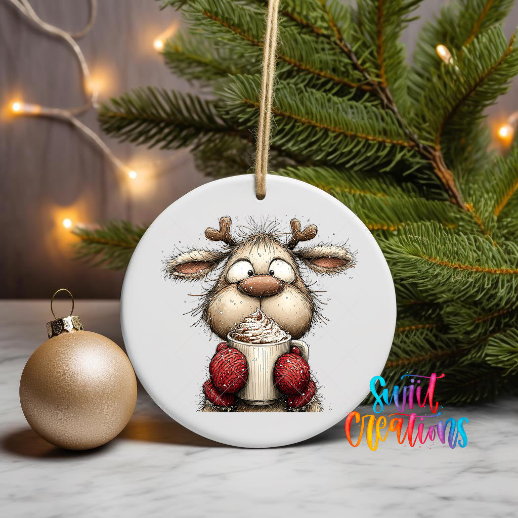 A white ceramic ornament featuring a cartoon reindeer holding a mug of hot chocolate, surrounded by Christmas lights and a pine tree.