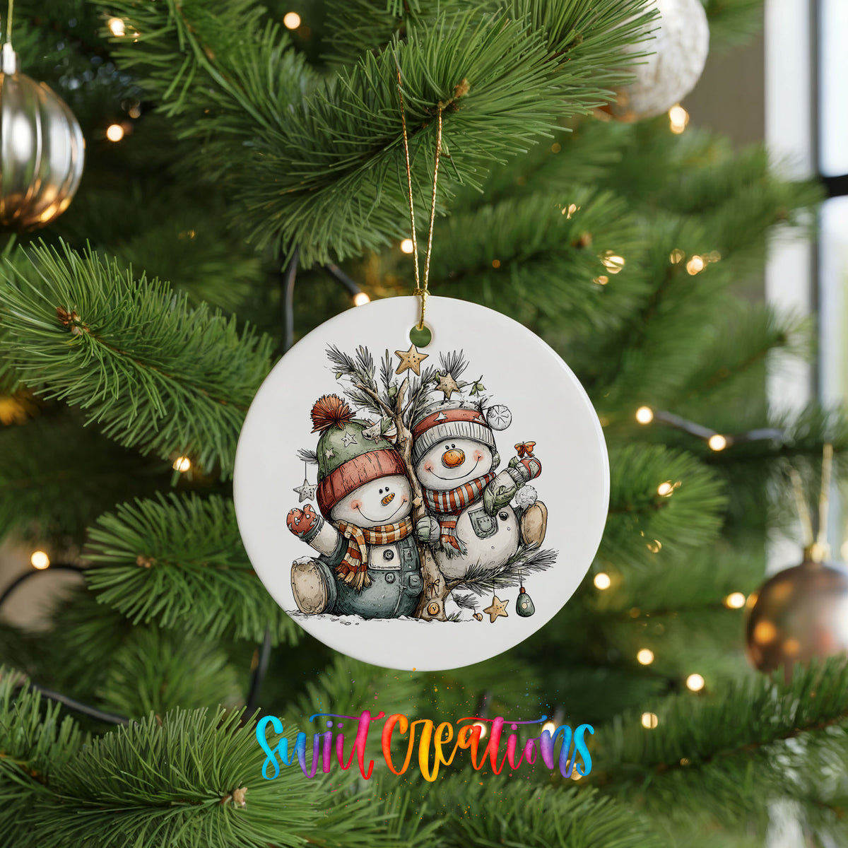 A white Christmas tree ornament featuring two snowmen, one wearing a green hat and the other a red hat, is hanging from the tree.