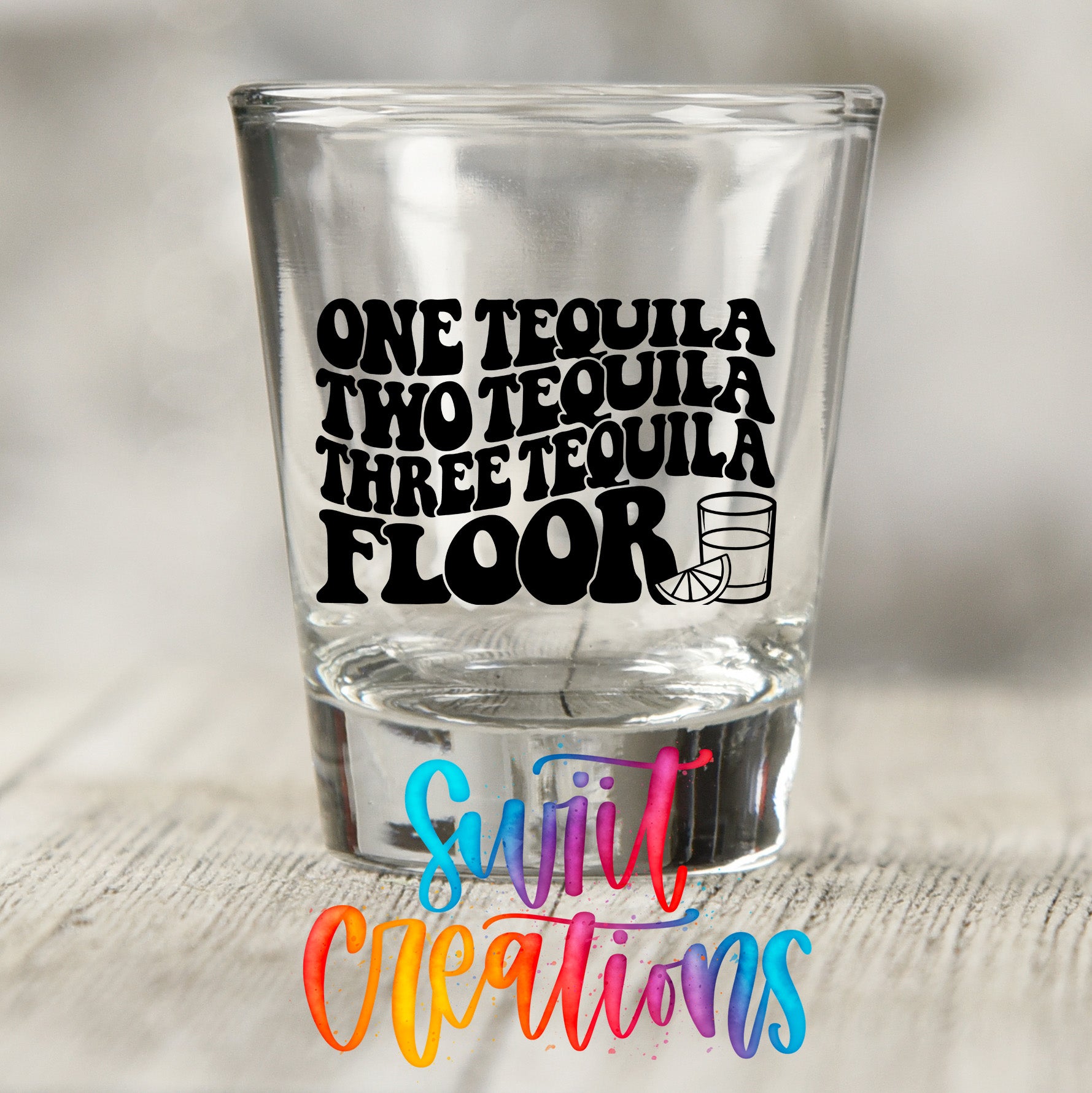 A clear shot glass with the text "ONE TEQUILA TWO TEQUILA THREE TEQUILA FLOOR" printed on it, along with a graphic of a tequila glass.