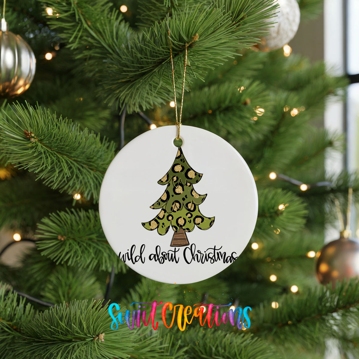 A white Christmas tree ornament with a leopard print design hangs from a tree branch, surrounded by other ornaments and twinkling lights.