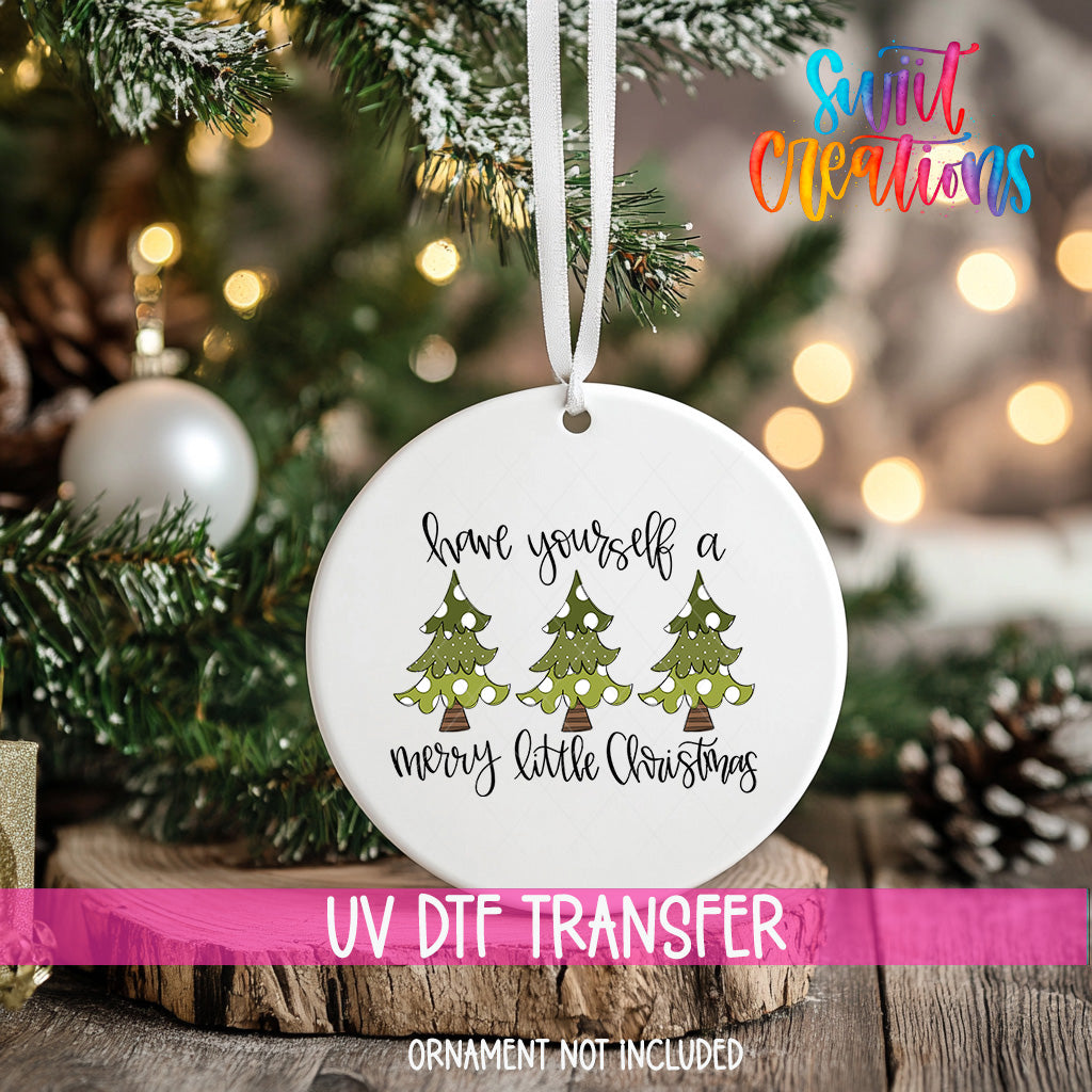 A white ceramic ornament with a Christmas tree design hangs on a tree branch, with a pink ribbon around it.