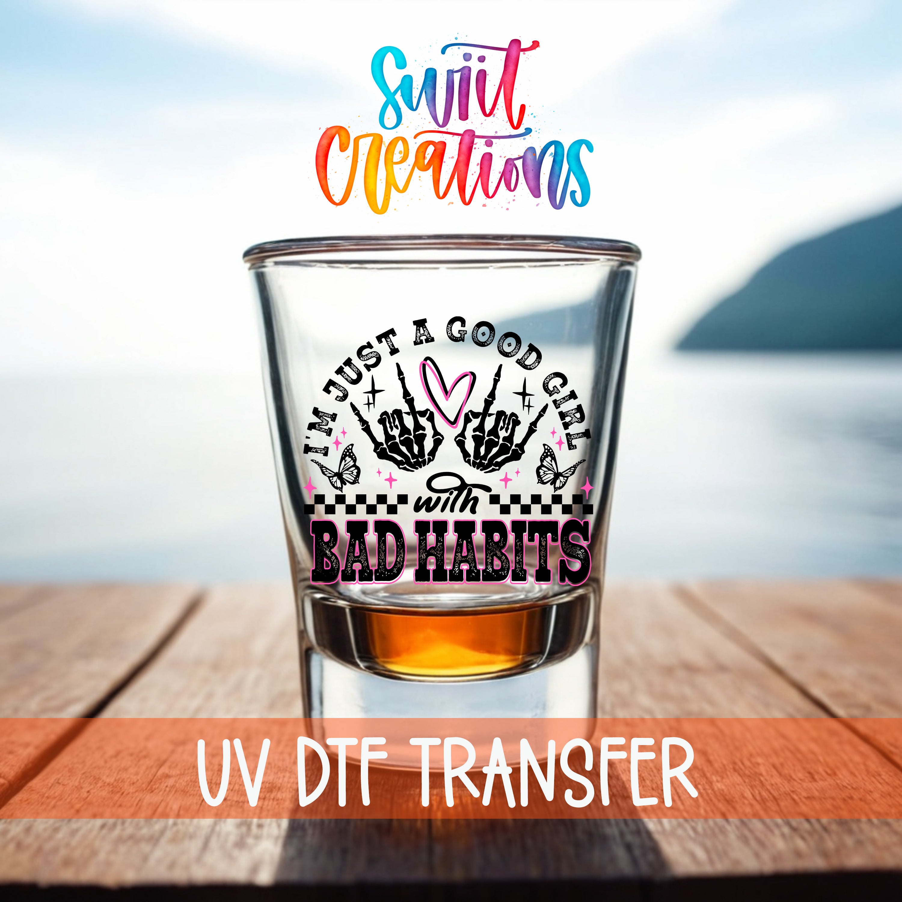 a shot glass with a colorful design and text, placed on a wooden surface with a body of water in the background.