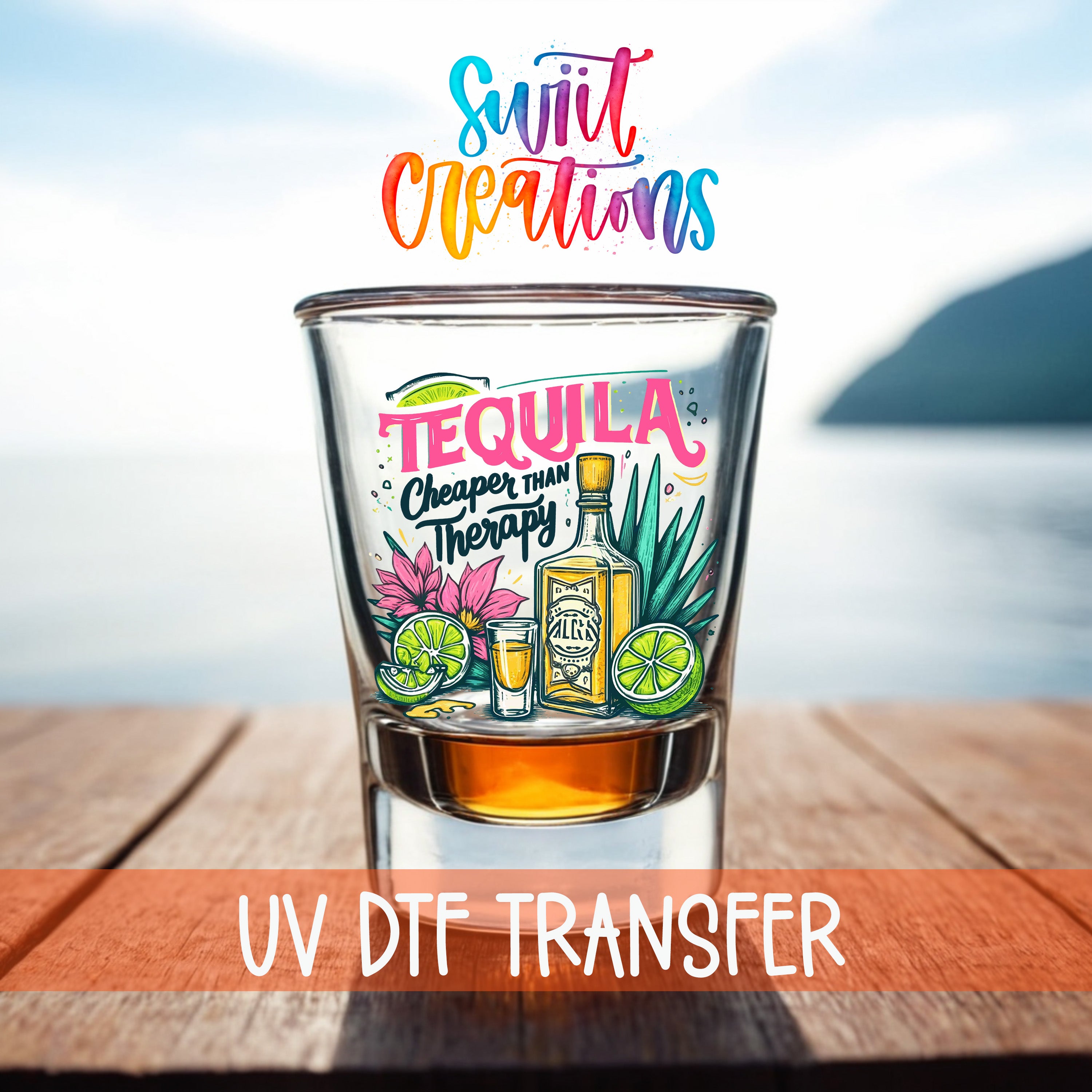 a glass of tequila with a colorful design, placed on a wooden surface with a body of water in the background.