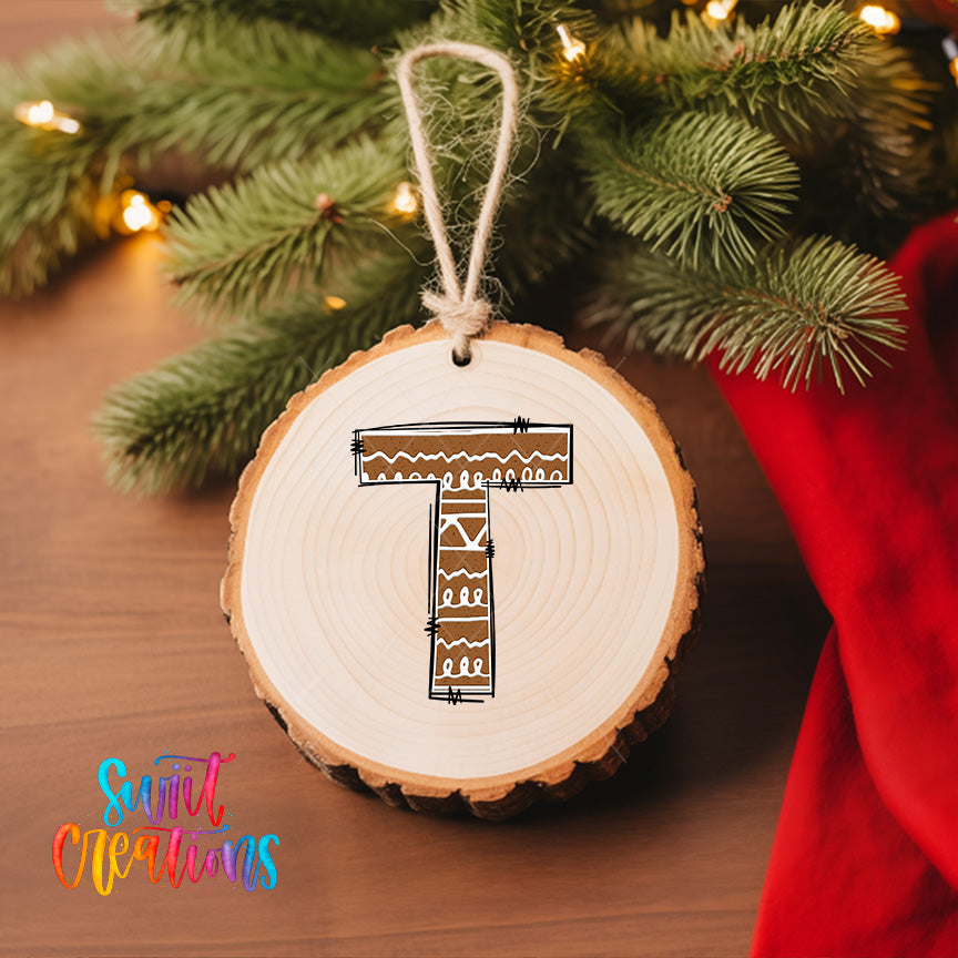 A wooden ornament with a letter "T" drawn on it, hanging on a Christmas tree.