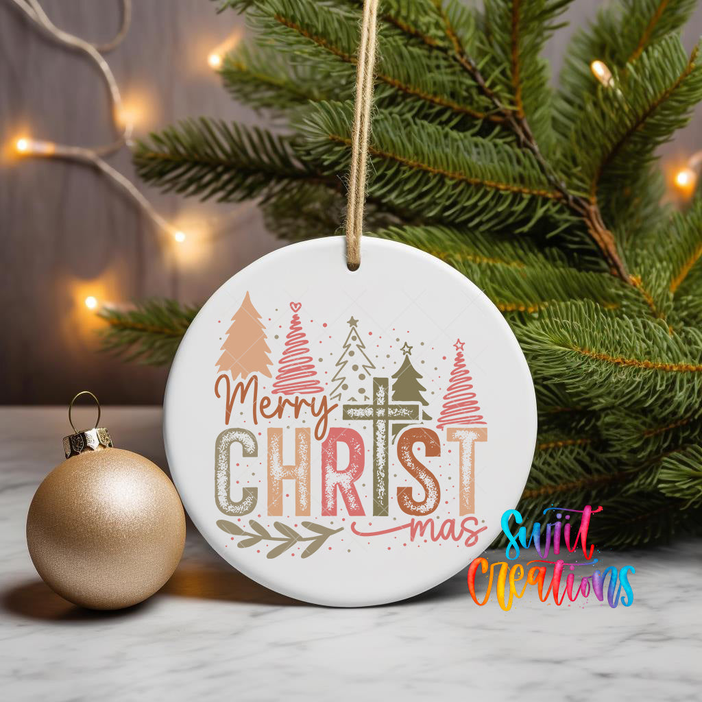 A white Christmas ornament with the text "Merry Christmas" and a design of Christmas trees and ornaments is displayed on a table, with a gold ornament and a pine tree in the background.