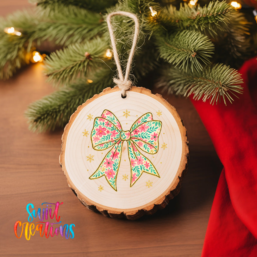 A wooden ornament with a bow and snowflakes is hanging on a Christmas tree, surrounded by pine branches and twinkling lights.