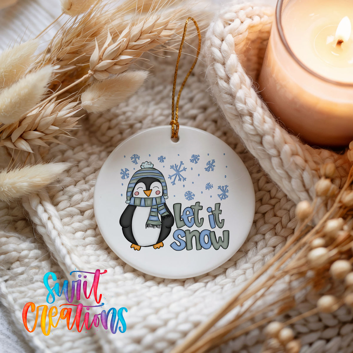A white ornament with a penguin wearing a scarf and hat, surrounded by snowflakes, and the text "Let it snow" is displayed on a knitted blanket.