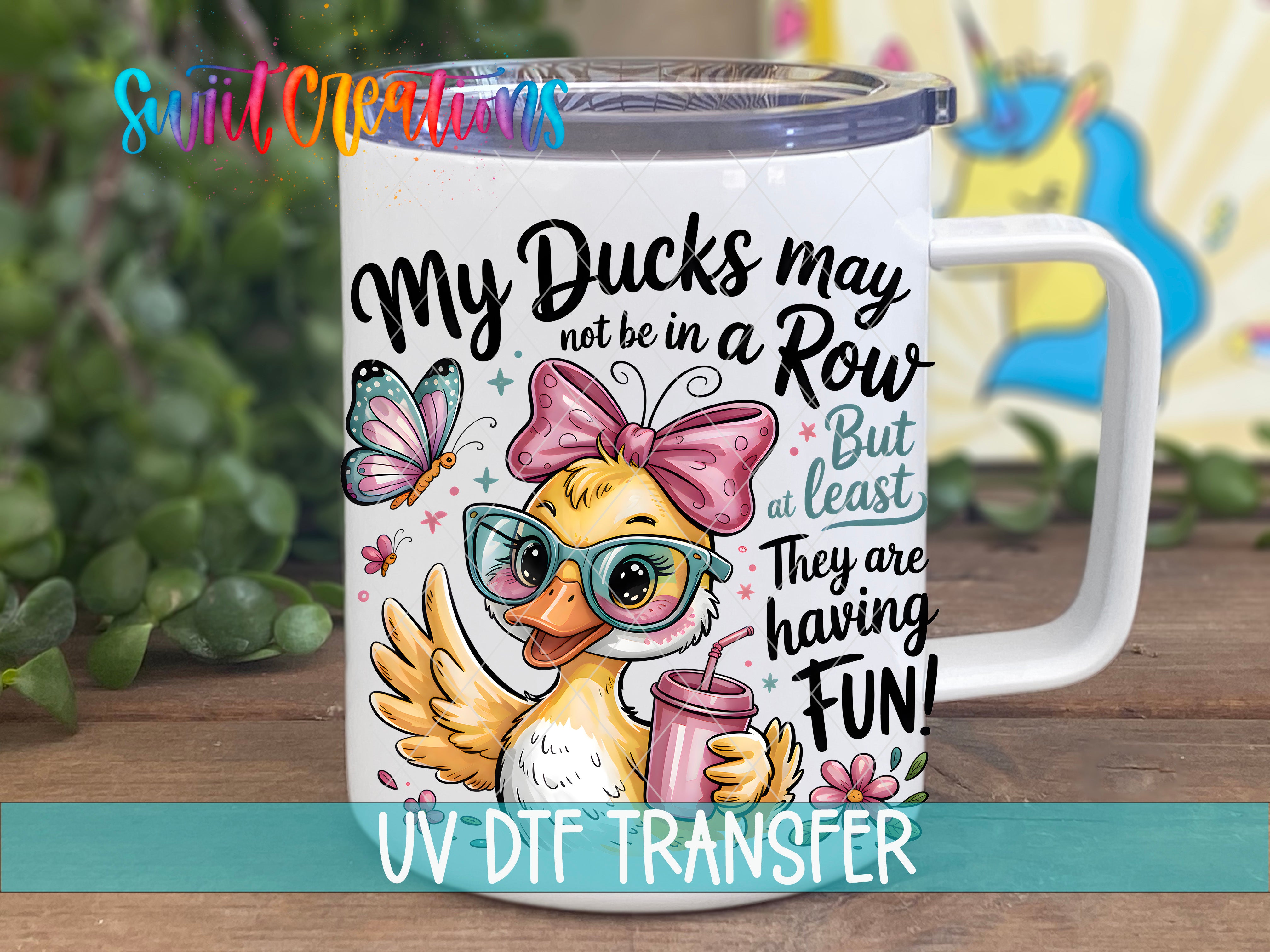 A white mug with a cartoon duck wearing glasses and a pink bow, along with text and illustrations, placed on a wooden surface.