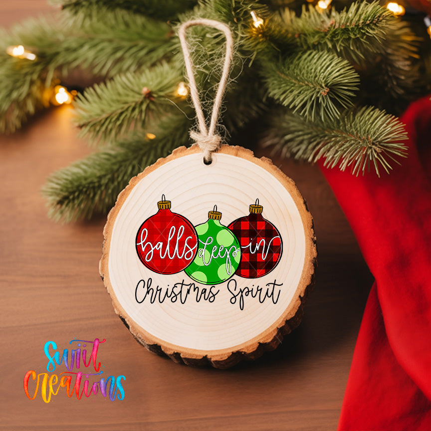 A wooden ornament with the text "balls keepin' in Christmas spirit" hanging on a Christmas tree, surrounded by pine branches and twinkling lights.