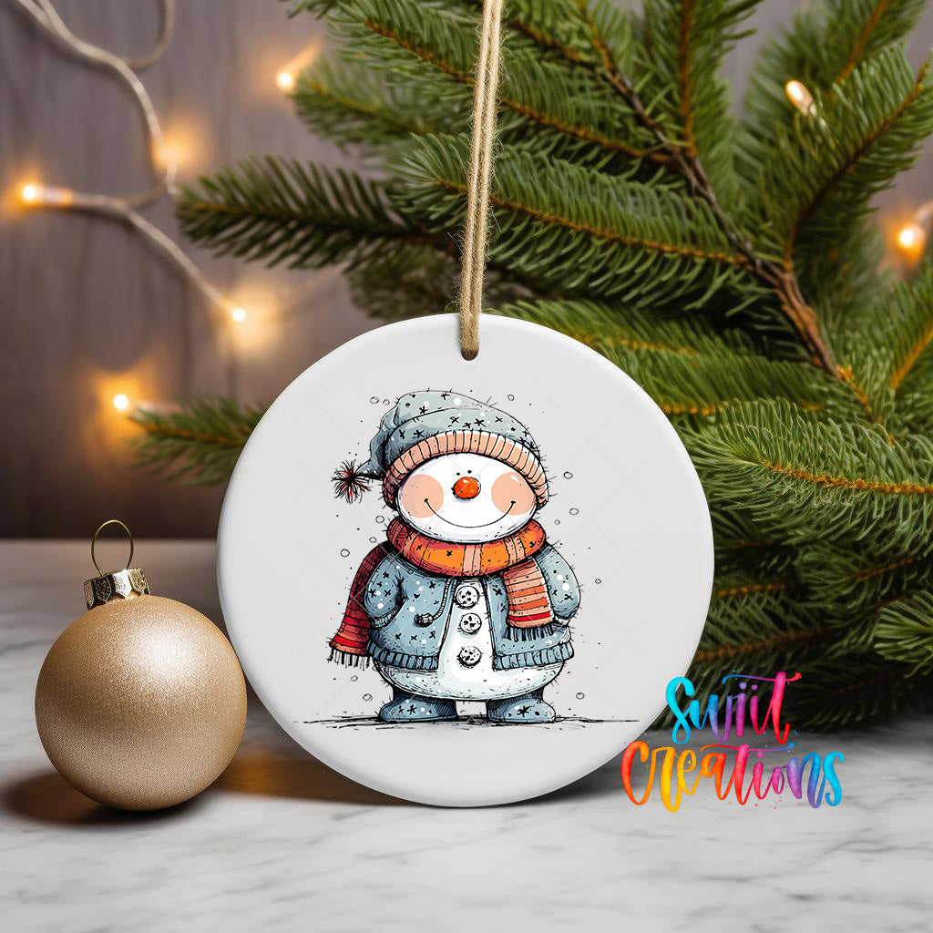 A white ceramic ornament featuring a snowman is displayed on a table, with a Christmas tree and a gold ornament in the background.