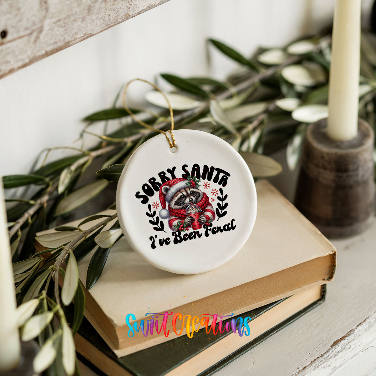Sorry Santa I've Been Feral funny raccoon ceramic Christmas ornament styled on books with holiday greenery