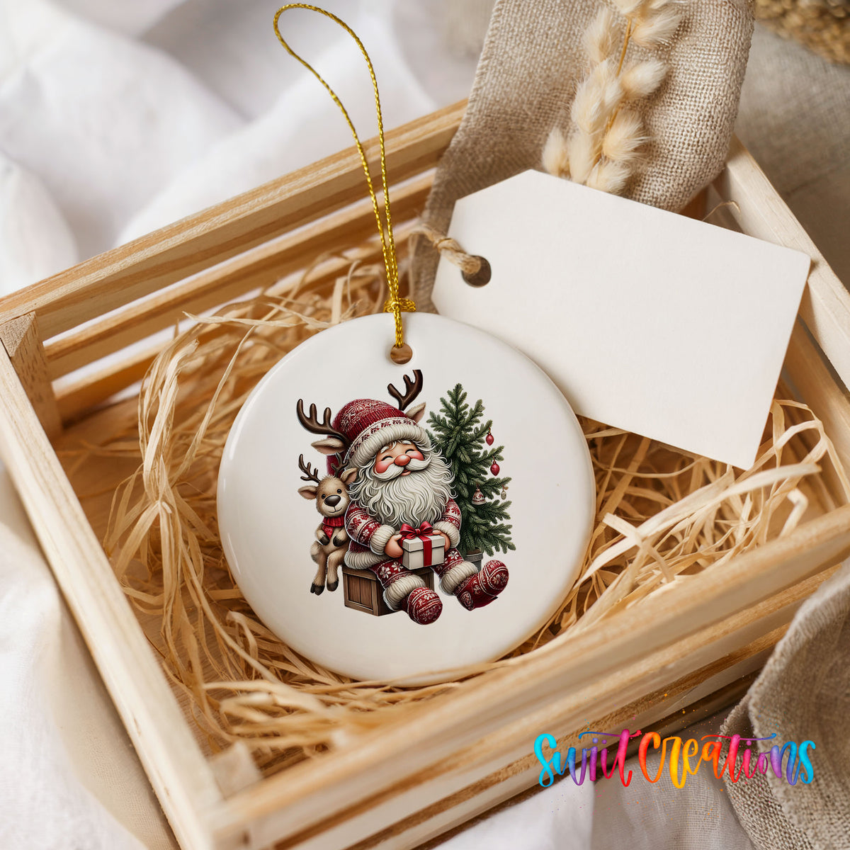 Round ceramic Christmas ornament featuring Santa with a reindeer beside a decorated Christmas tree, presented in a rustic wooden gift crate
