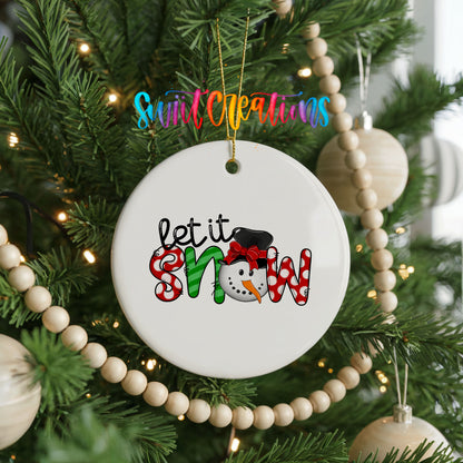 Round ceramic Christmas ornament featuring playful red and black Let It Snow holiday typography, hanging on a decorated Christmas tree