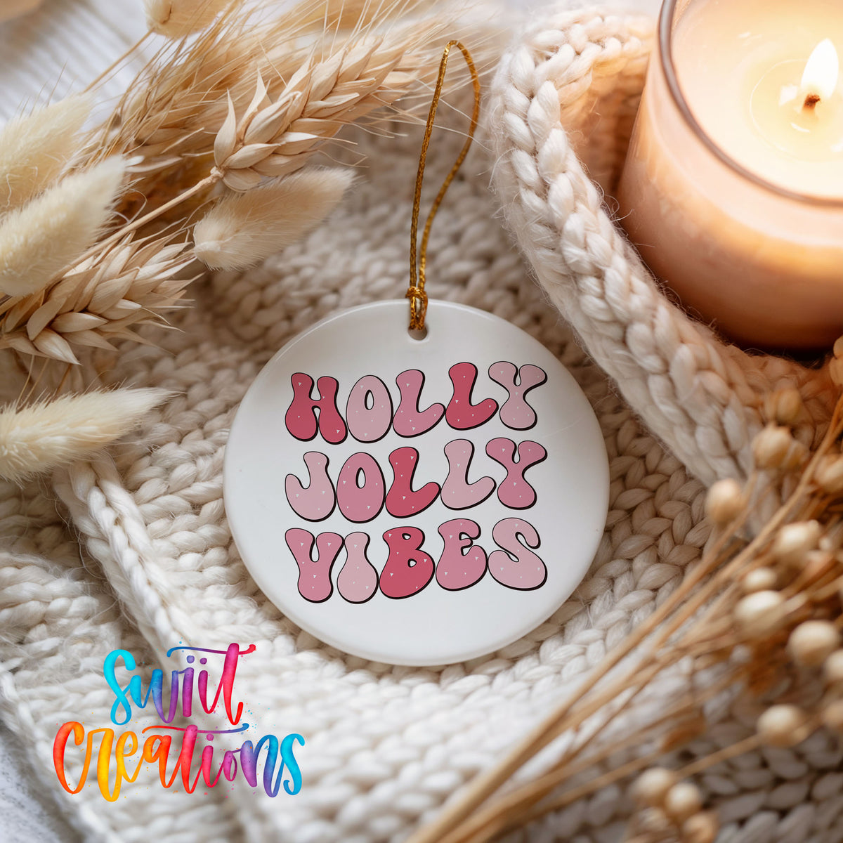 Round ceramic Christmas ornament featuring pink retro Holly Jolly Vibes typography, styled beside a candle and cozy knit blanket