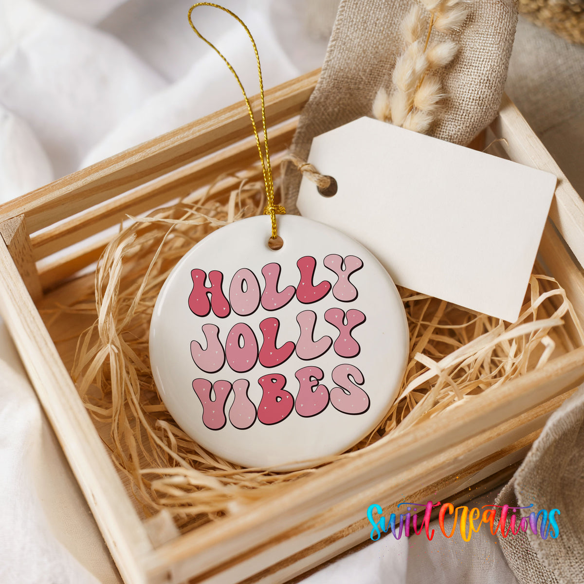 Round ceramic Christmas ornament featuring pink retro Holly Jolly Vibes typography, presented in a rustic wooden gift crate
