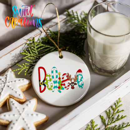 Round ceramic Christmas ornament featuring colorful whimsical Believe holiday lettering, styled with cookies and milk