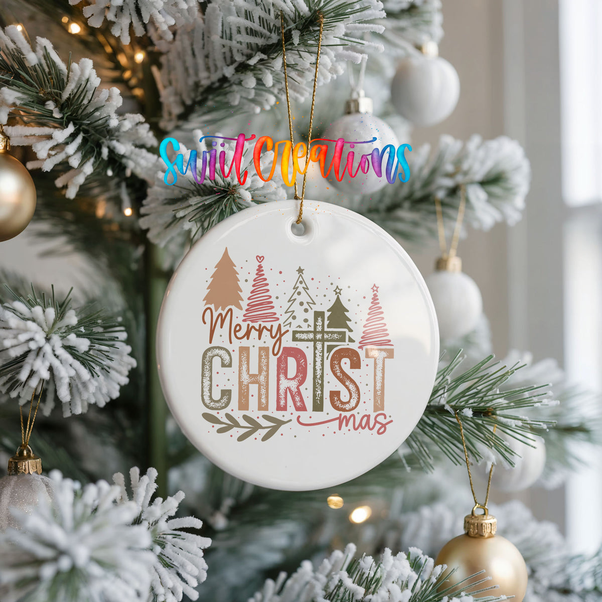 Round ceramic Christmas ornament featuring Merry Christmas typography with a pastel winter village and trees, hanging on a frosted Christmas tree