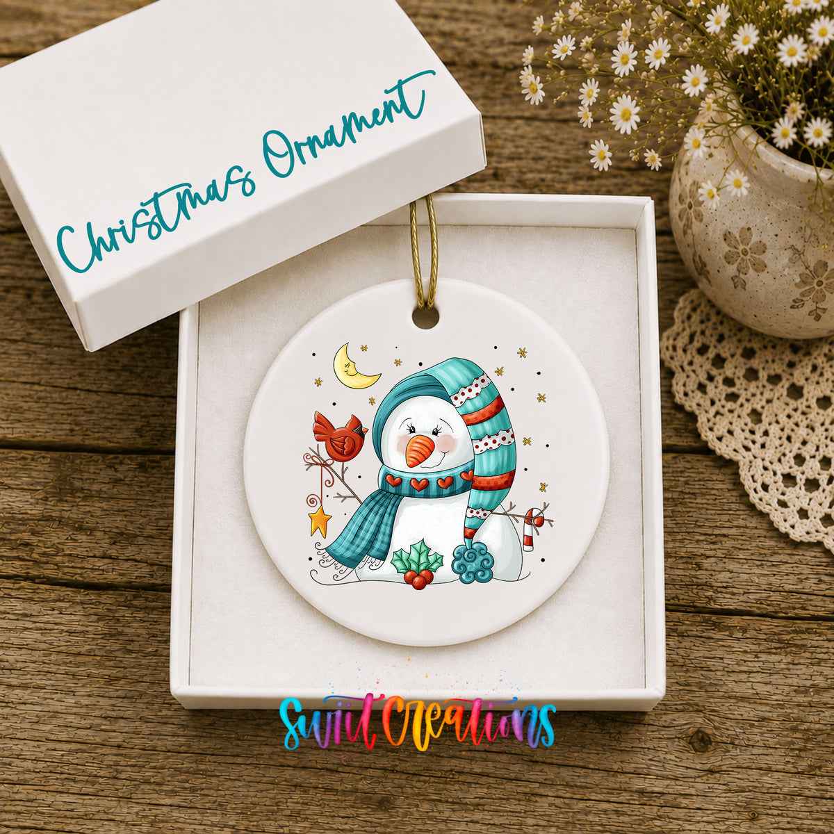 Round ceramic Christmas ornament featuring cozy snowman holding a bright red cardinal beneath a winter moon, displayed in the included gift box