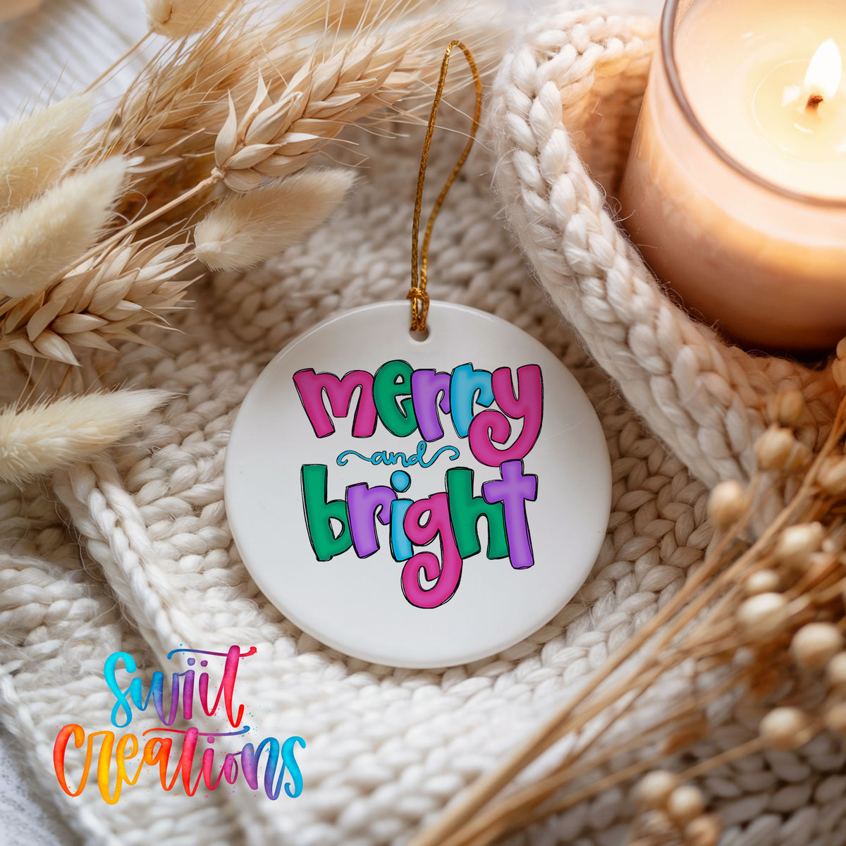 Round ceramic Christmas ornament featuring bright groovy Merry and Bright lettering in pink teal and purple, styled beside a candle and cozy knit blanket