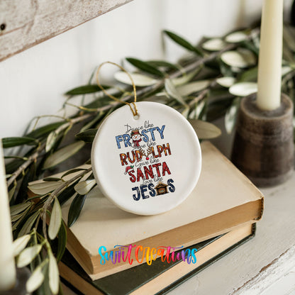 Round ceramic Christmas ornament featuring Dance like Frosty ride like Rudolph give like Santa love like Jesus message, styled on books with holiday greenery