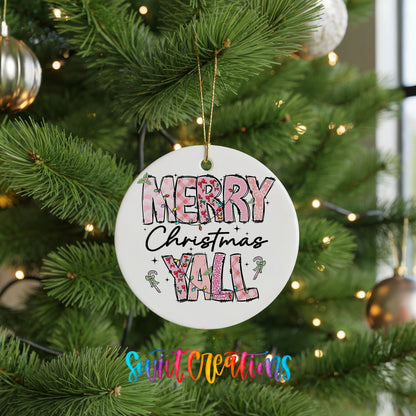 Round ceramic Christmas ornament featuring patterned Merry Christmas Y’all lettering with pink and green accents, hanging on a green Christmas tree