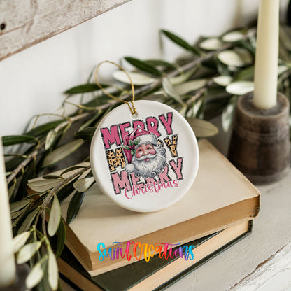 Round ceramic Christmas ornament featuring stacked Merry Merry Merry Christmas lettering with Santa and leopard print accents, styled on books with holiday greenery