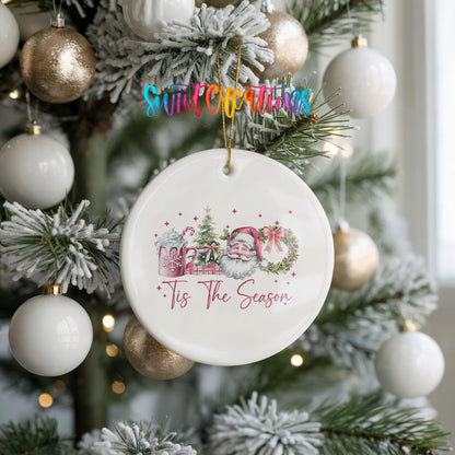 Round ceramic Christmas ornament featuring vintage Santa with floral greenery and ’Tis the Season lettering, hanging on a frosted holiday tree