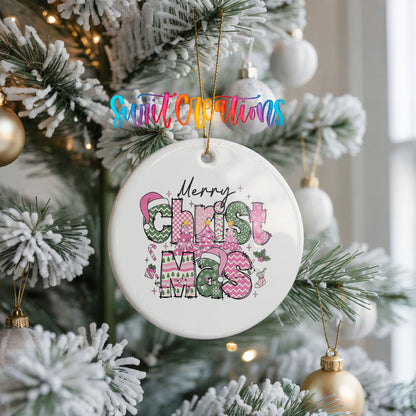 Round ceramic Christmas ornament featuring stacked patterned Merry Christmas lettering in pink green and black, hanging on a frosted Christmas tree